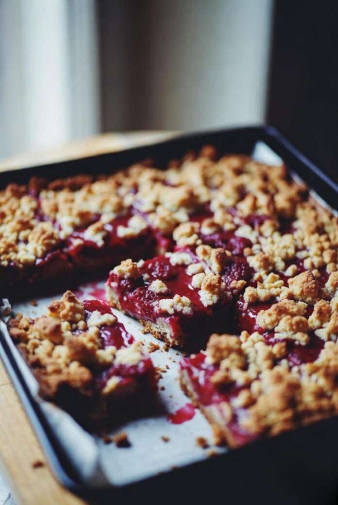 slightly vintage-filtered shot of a rustic tray of Raspberry Crumble Bars, unevenly sliced, bright raspberry filling oozing slightly. slightly vintage-filtered shot of a rustic tray of Raspberry Crumble Bars, unevenly sliced, bright raspberry filling oozing slightly.