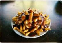 ⭐ Poutine Recipe That Totally Wrecked My Life a messy plate of poutine on a scratched diner table.