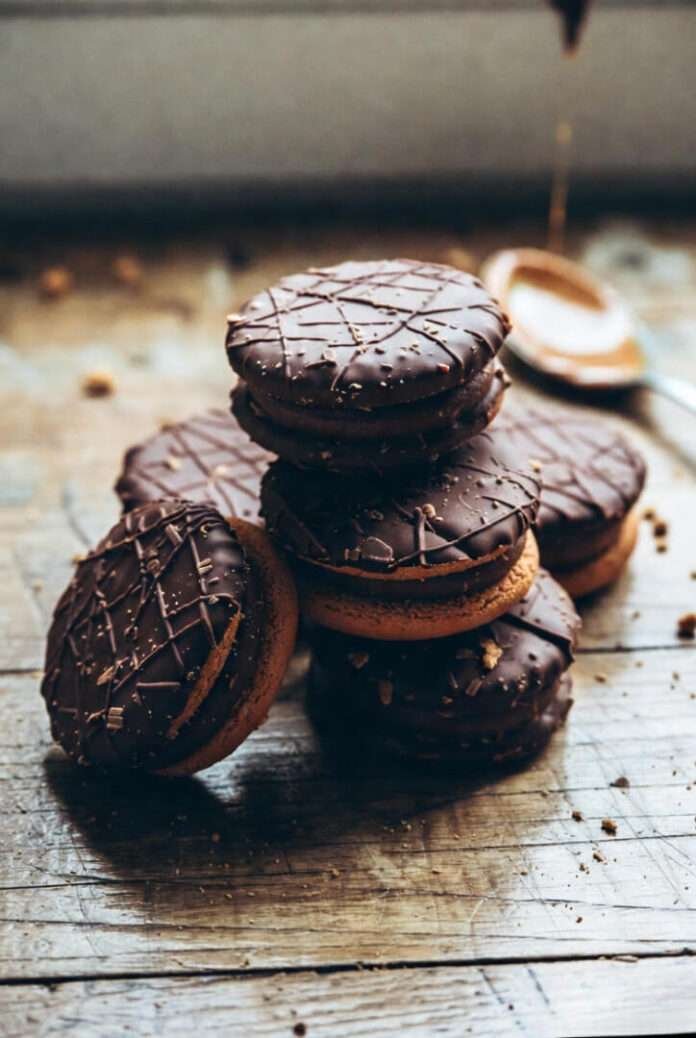 A stack of chocolate alfajores on a weathered wooden table, soft window light from the side, crumbs everywhere A stack of chocolate alfajores on a weathered wooden table, soft window light from the side, crumbs everywhere