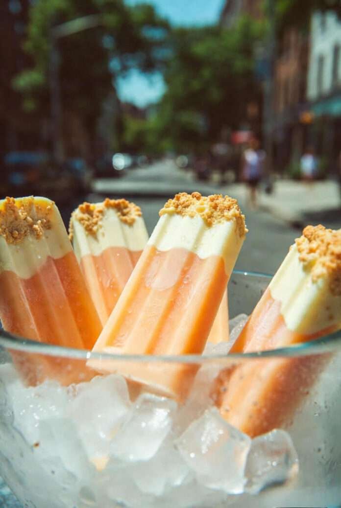 A dreamy, sunlit shot of several Peach Crisp Parfait Pops leaning against a frosty glass bowl filled with ice. A dreamy, sunlit shot of several Peach Crisp Parfait Pops leaning against a frosty glass bowl filled with ice.