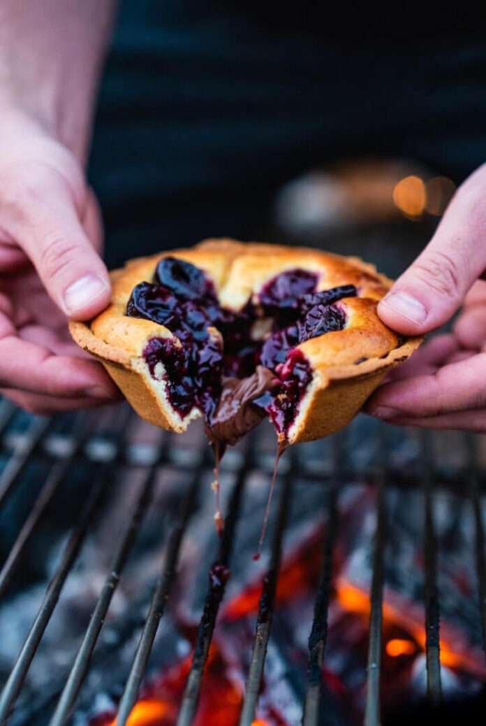 a gooey cherry-chocolate pudgy pie being pulled apart by two hands over a small campfire grate. a gooey cherry-chocolate pudgy pie being pulled apart by two hands over a small campfire grate.