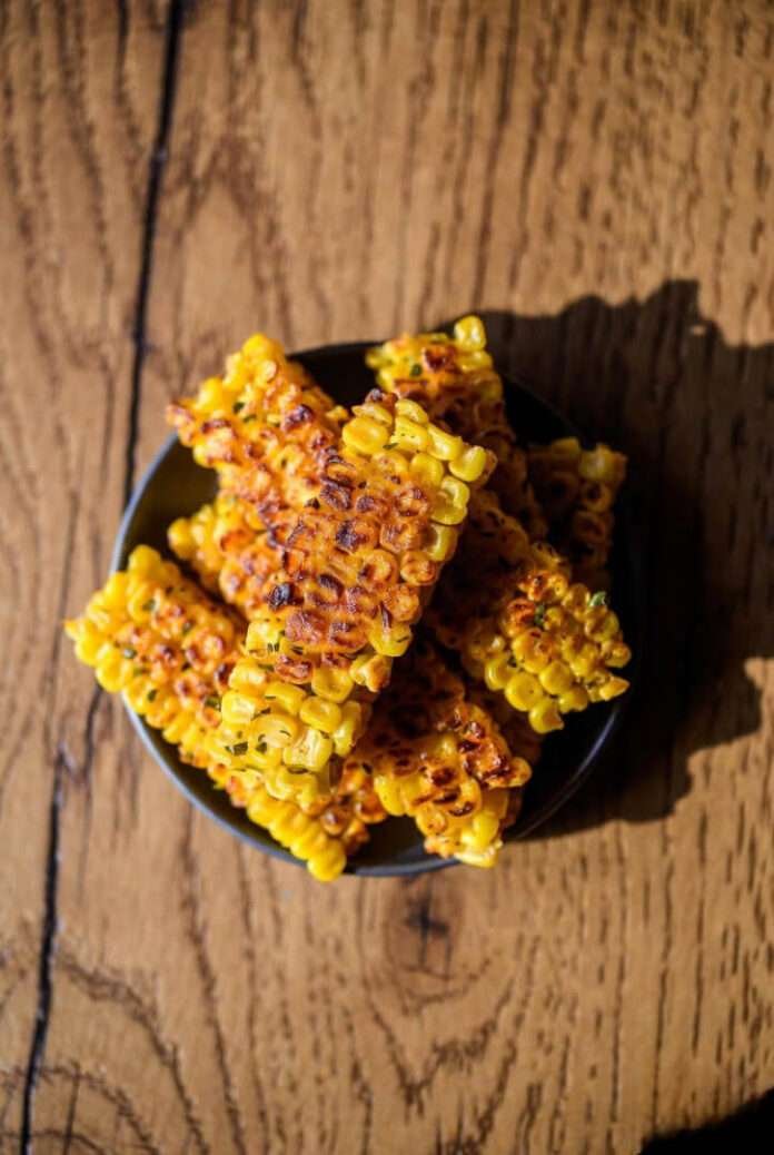 a plate of crispy corn kebabs on a textured wooden table, warm lighting, a little shadow on the right for depth. a plate of crispy corn kebabs on a textured wooden table, warm lighting, a little shadow on the right for depth.