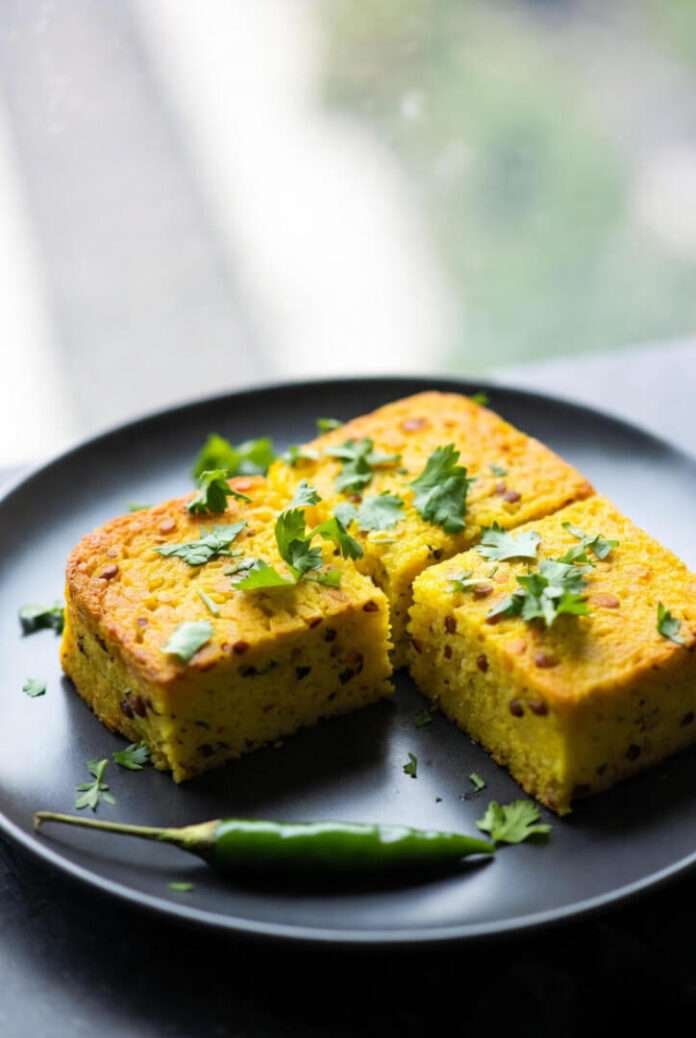 freshly steamed Moong Dal Dhokla cut into squares, arranged imperfectly on a matte black plate. freshly steamed Moong Dal Dhokla cut into squares, arranged imperfectly on a matte black plate.