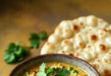 Matar Kulcha Recipe That’ll Make You Miss Delhi Even If You’ve Never Been a rustic bowl of matar curry with soft kulchas on the side. Slightly blurred photorealistic style. Warm lighting.